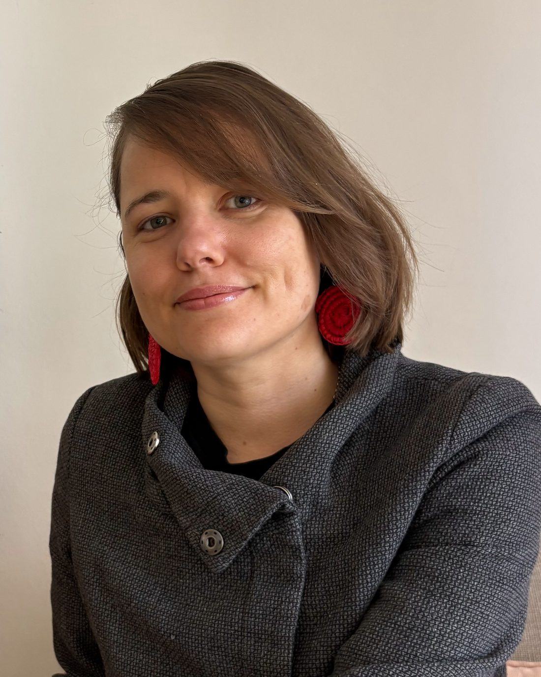 Miranda Brockhurst, smiling, wearing a grey jacket and red earrings
